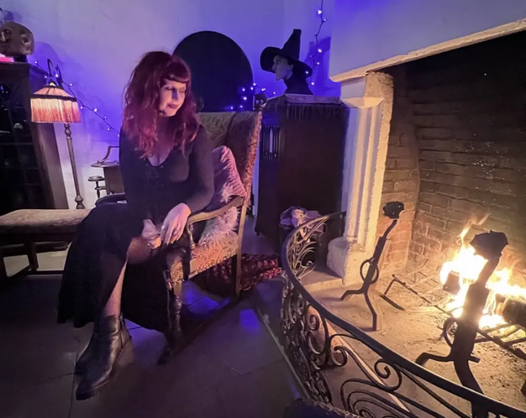 Scarlett Amaris seated beside a lit stone fireplace in a blue-lit room.